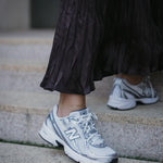 Нови спортни обувки New Balance в комбинация с дълга, plisирана пола, стъпала на стълби.