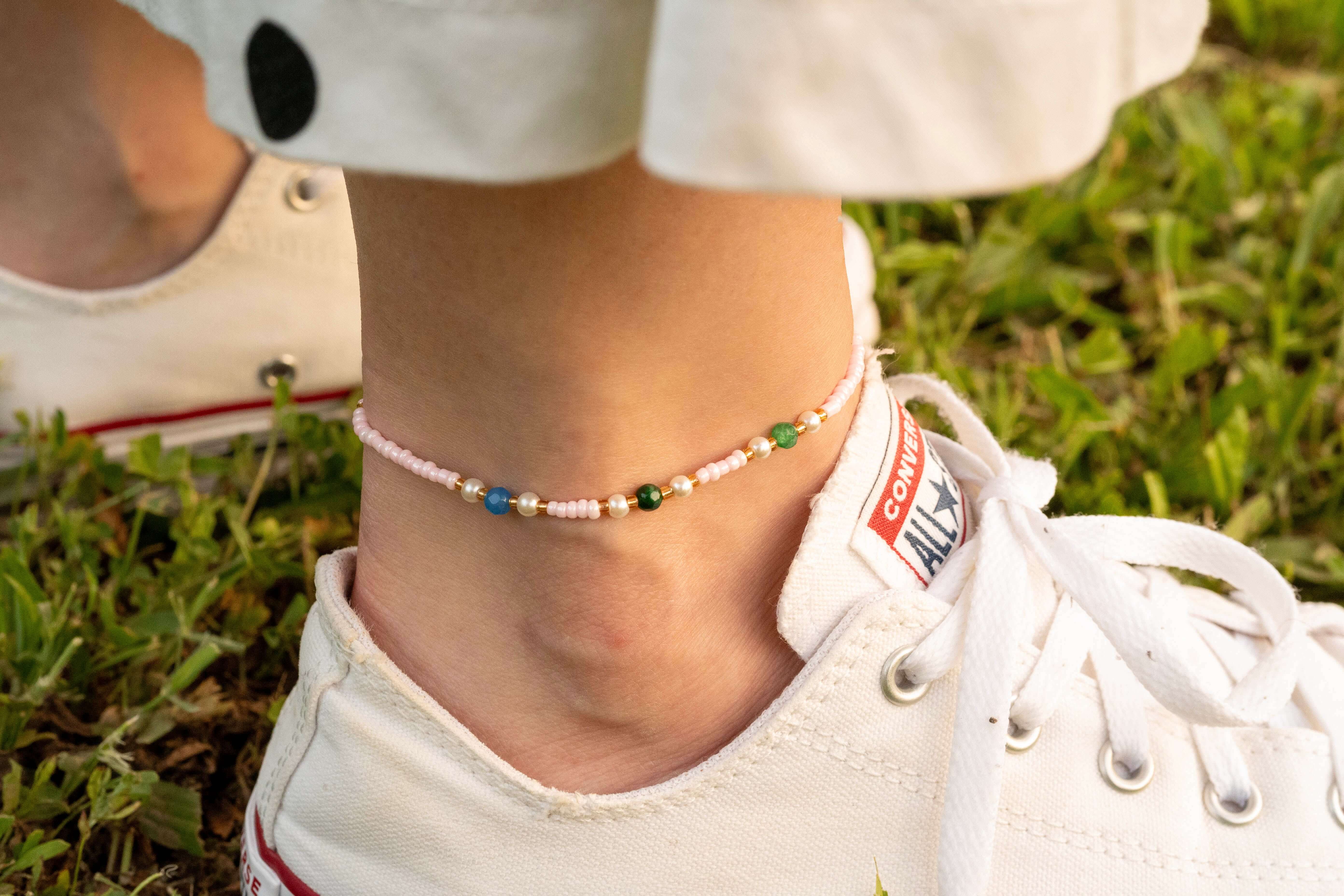 Бохо гривна за глезен с цветни мъниста, носена с летни обувки на тревна повърхност.