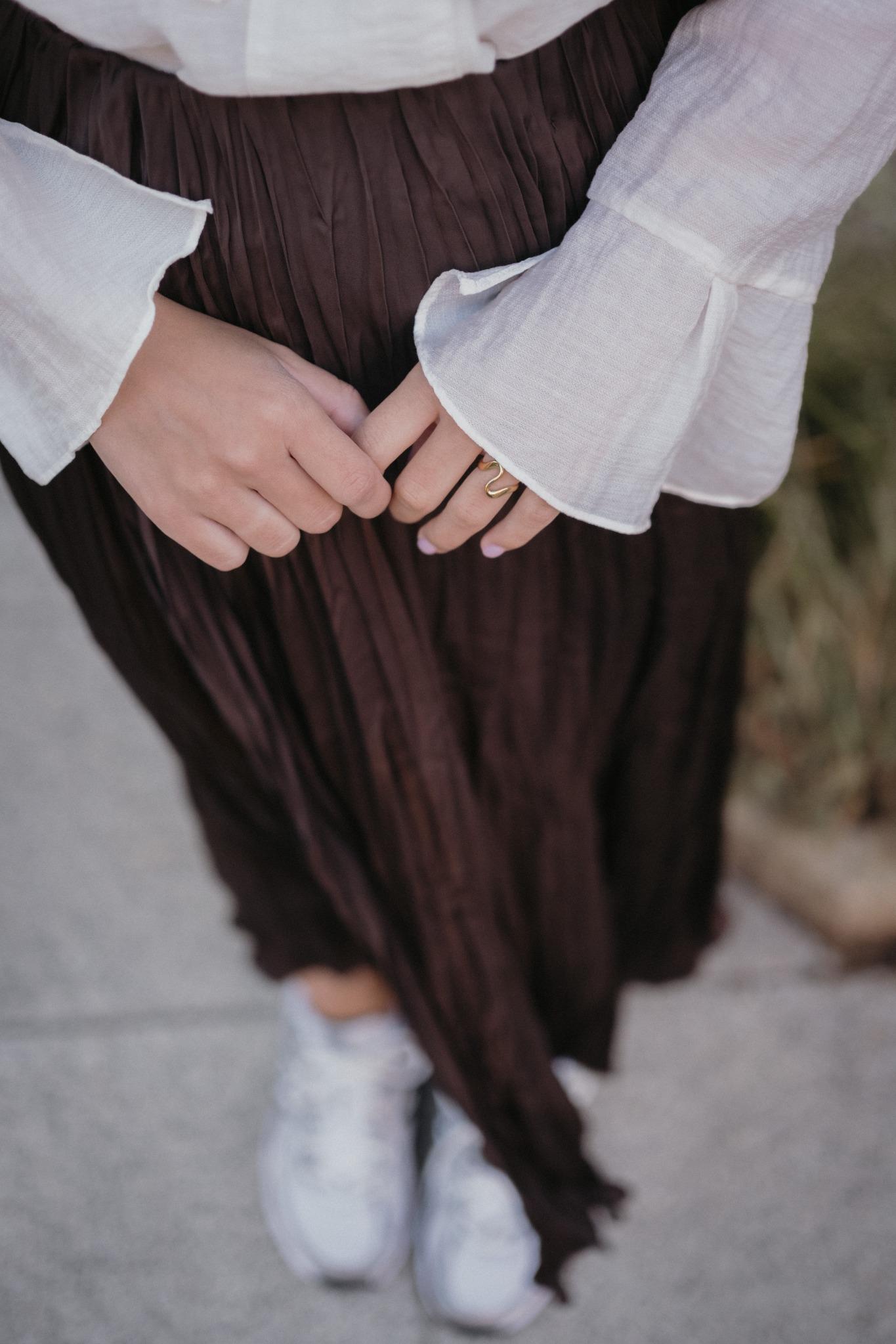 стилна жена с златист пръстен Wave и кремава риза, носеща къса пола на улицата