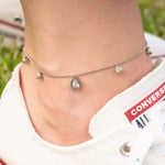 Гривна за глезен с блестящи циркониеви камъни, носена с спортни обувки на зелена трева.