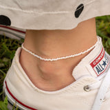 Лека гривна за глезен с цветни мъниста, носена с удобни мокасини на трева.