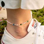 Бохо гривна за глезен с цветни мъниста, носена с летни обувки на тревна повърхност.