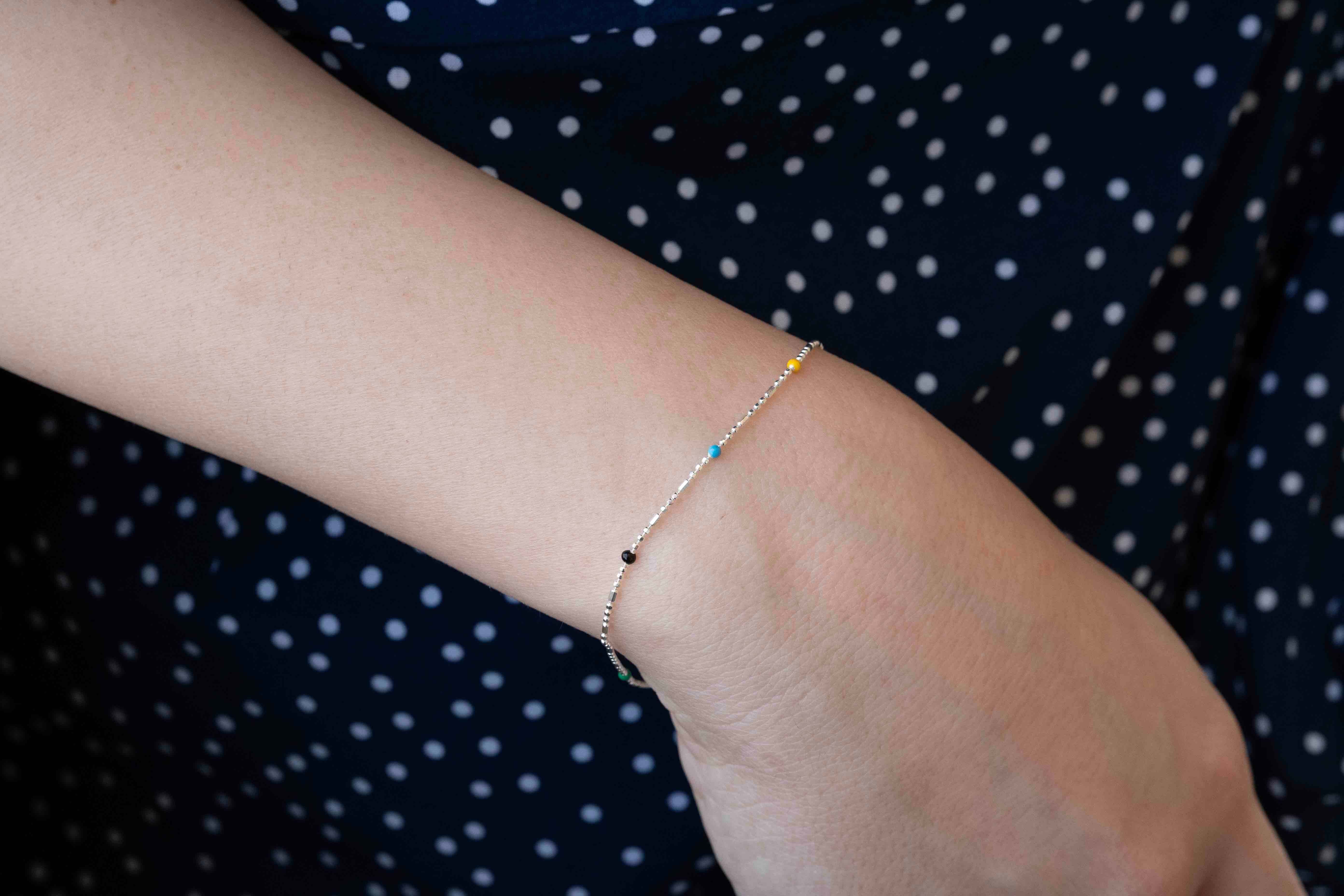 Сребърна гривна S925 с многоцветни елементи върху ръката на човек, носеща стилна дреха.