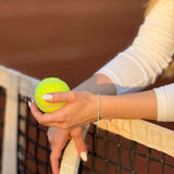 Жена държи тенис топка в ръка, докато се опира на тенис мрежа.