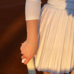 Ръка с тенис ракета, носеща елегантна бяла пола и тънка гривна на тенис корта.