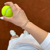 Длан, държаща тенис топка, с тенис гривна от неръждаема стомана и 18К златно покритие.