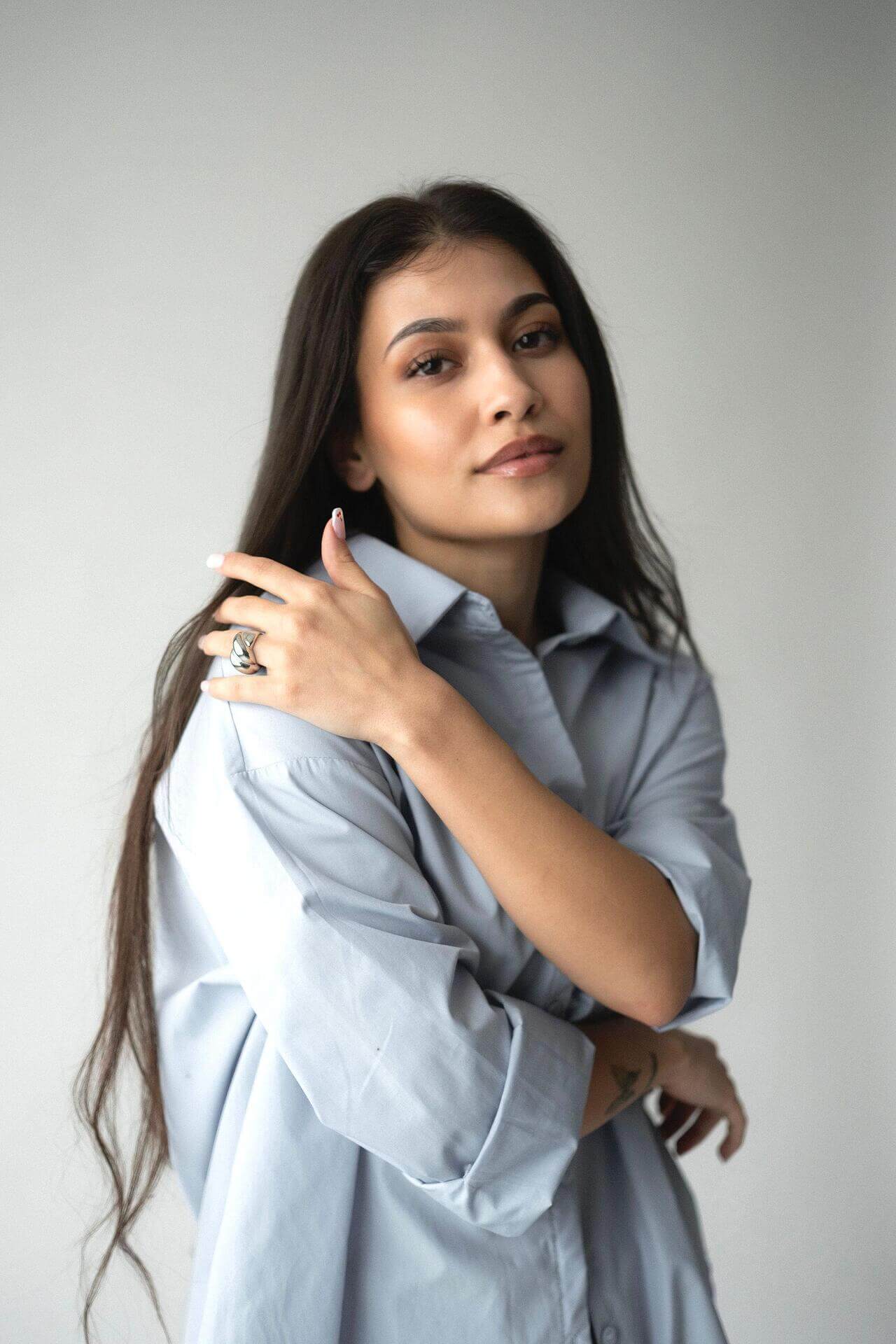 Млада жена с дълга коса носи chunky пръстен с 18К златно покритие, облечена в светлосиня риза.