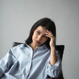 Woman in a blue shirt sitting on a chair, with long dark hair, appearing thoughtful.