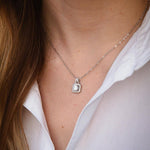 Елегантно сребърно колие с блестящи камъни, носено на жена с бяла риза.