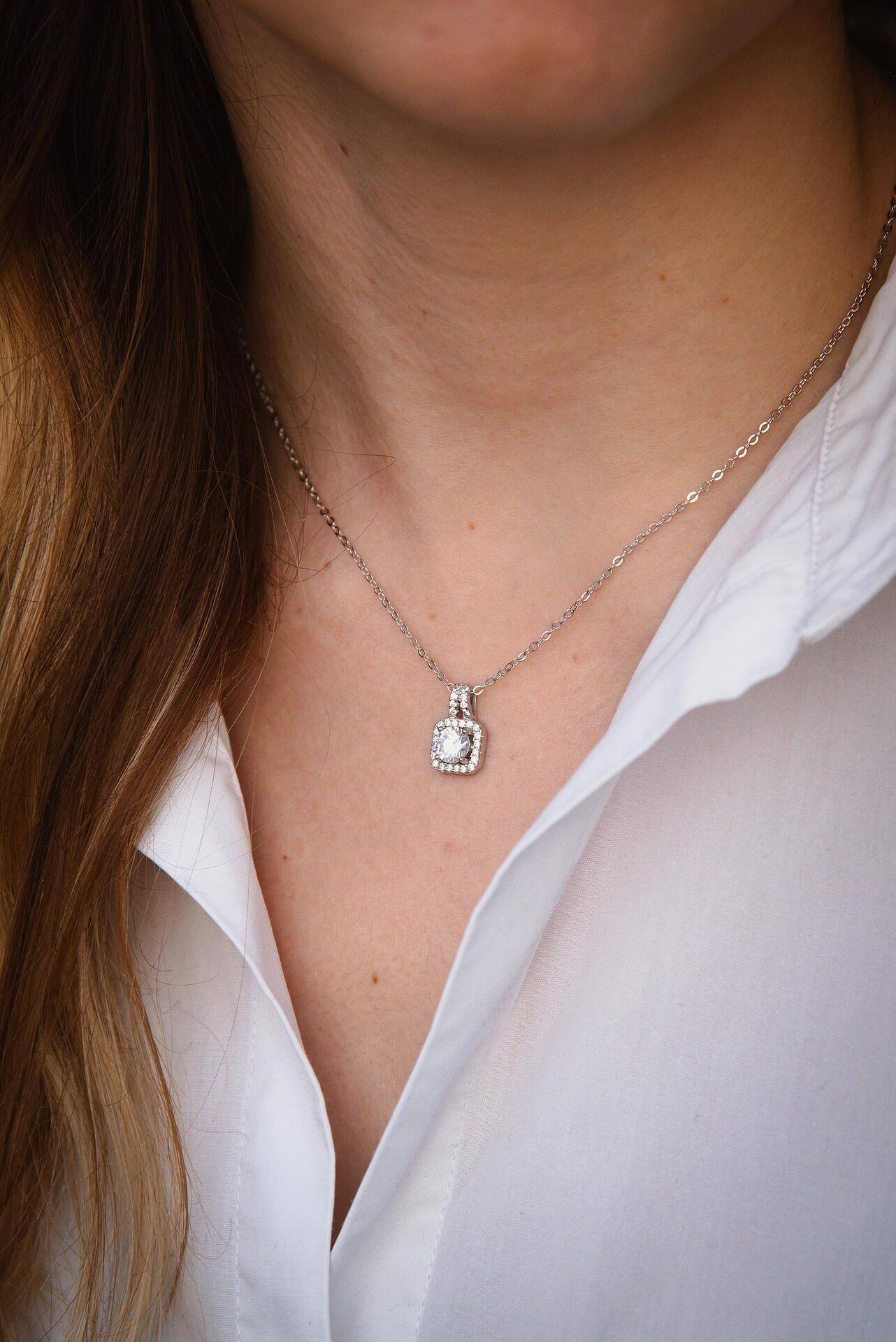 Елегантно сребърно колие с блестящи камъни, носено на жена с бяла риза.