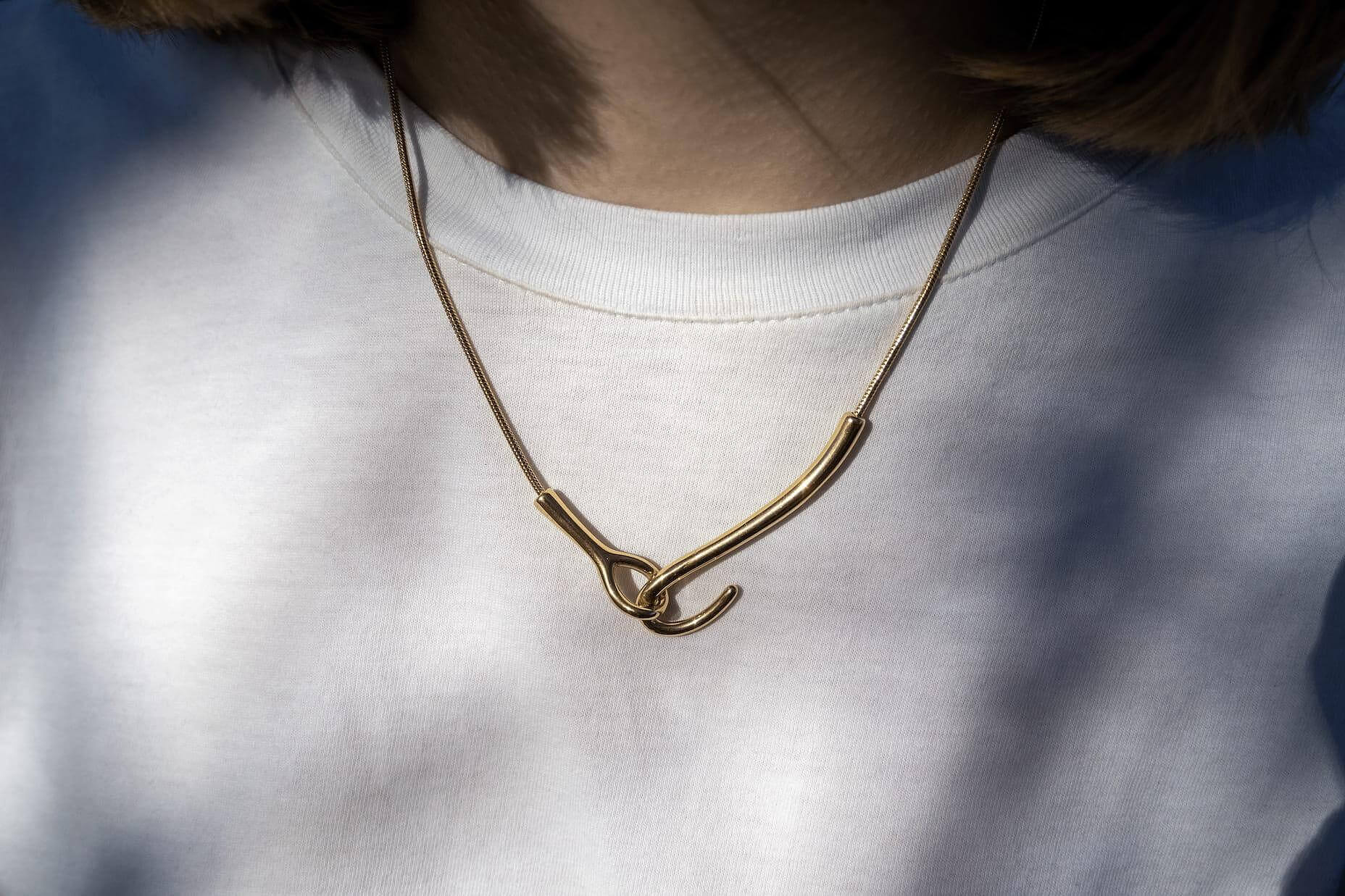 Златисто колие с уникален дизайн, носено върху бяла тениска, символизиращо елегантност и съвременен стил.