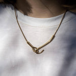 Златисто колие с уникален дизайн, носено върху бяла тениска, символизиращо елегантност и съвременен стил.