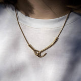 Златисто колие с уникален дизайн, носено върху бяла тениска, символизиращо елегантност и съвременен стил.