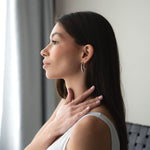 Elegant woman showcasing Обеци Течна Капка in gold, highlighting their shine and design by a window.