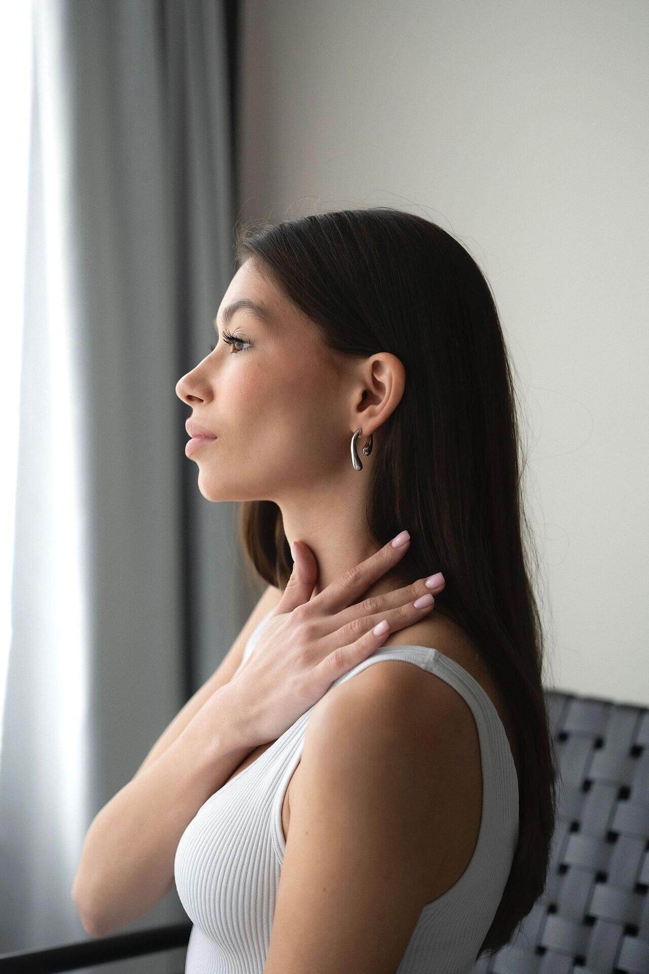 Elegant woman showcasing Обеци Течна Капка in gold, highlighting their shine and design by a window.