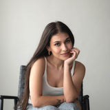 Young woman sitting in a chair with long hair, wearing a casual outfit, smiling thoughtfully at the camera.
