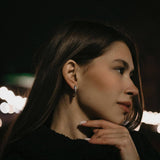 Жена с дълга коса, носеща обеци V-Shape в тъмен фон с светлини на заден план.