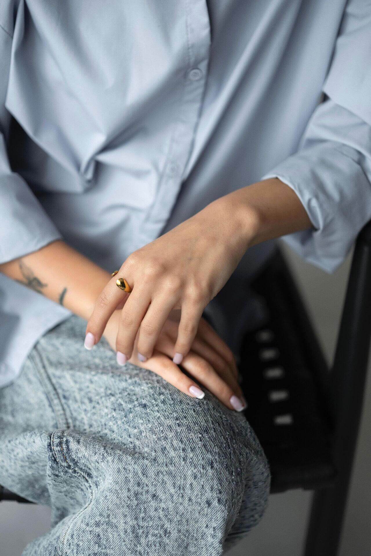 Woman wearing SOLIS ring with 18K gold plating, stylish fabric shirt, and casual jeans, showcasing luxury and warmth.