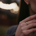 Сребърен пръстен с диамант и цирконий, носен от жена на фона на размити светлини.