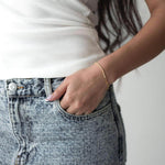 Жена с бели потници и дънки, носеща сребърна гривна с 18K златно покритие.