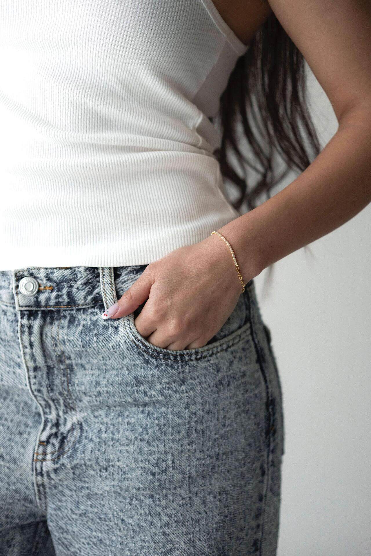 Жена с бели потници и дънки, носеща сребърна гривна с 18K златно покритие.