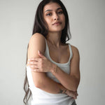Stylish young woman wearing a white tank top and jeans, showcasing a delicate silver bracelet against a neutral background.