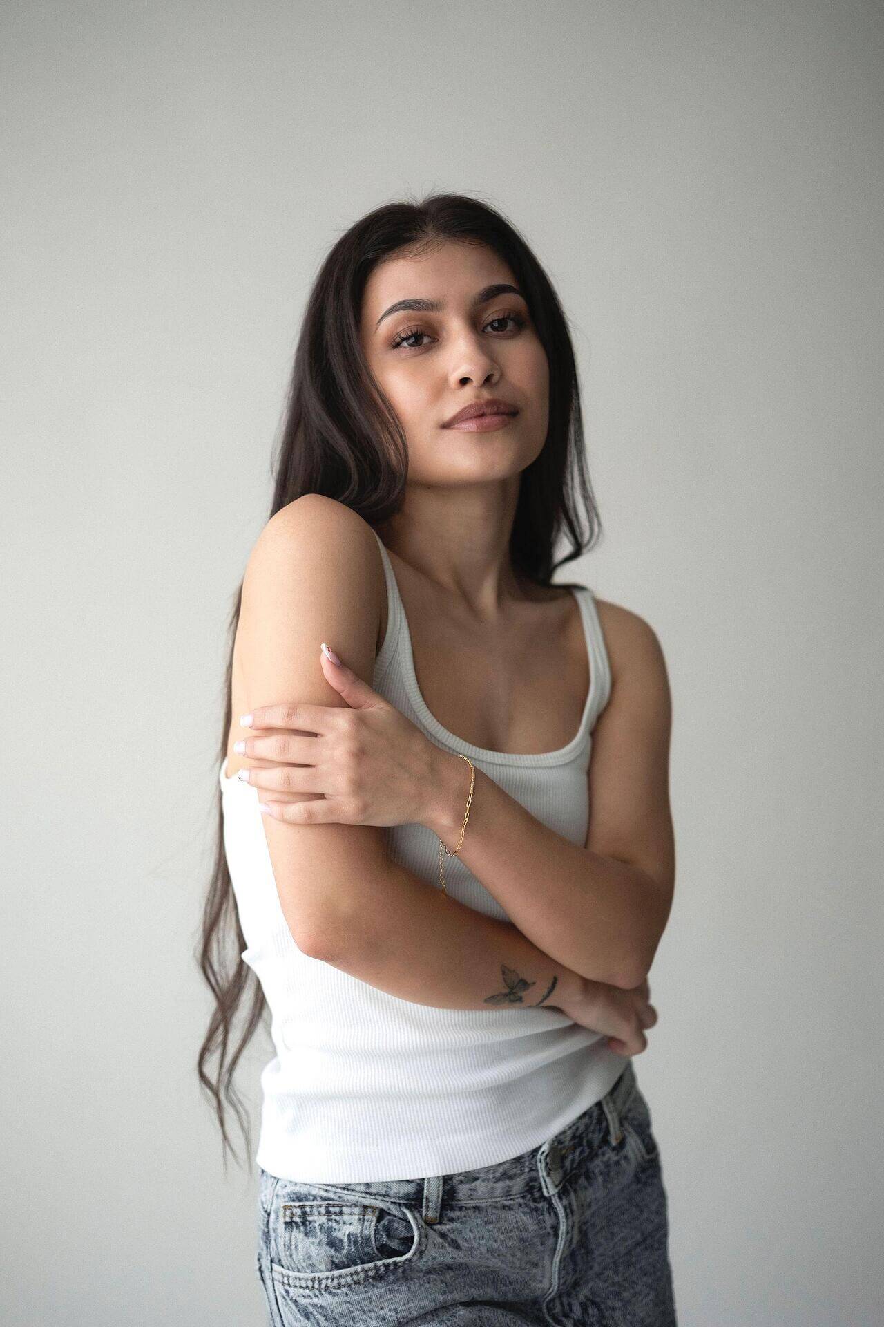 Stylish young woman wearing a white tank top and jeans, showcasing a delicate silver bracelet against a neutral background.