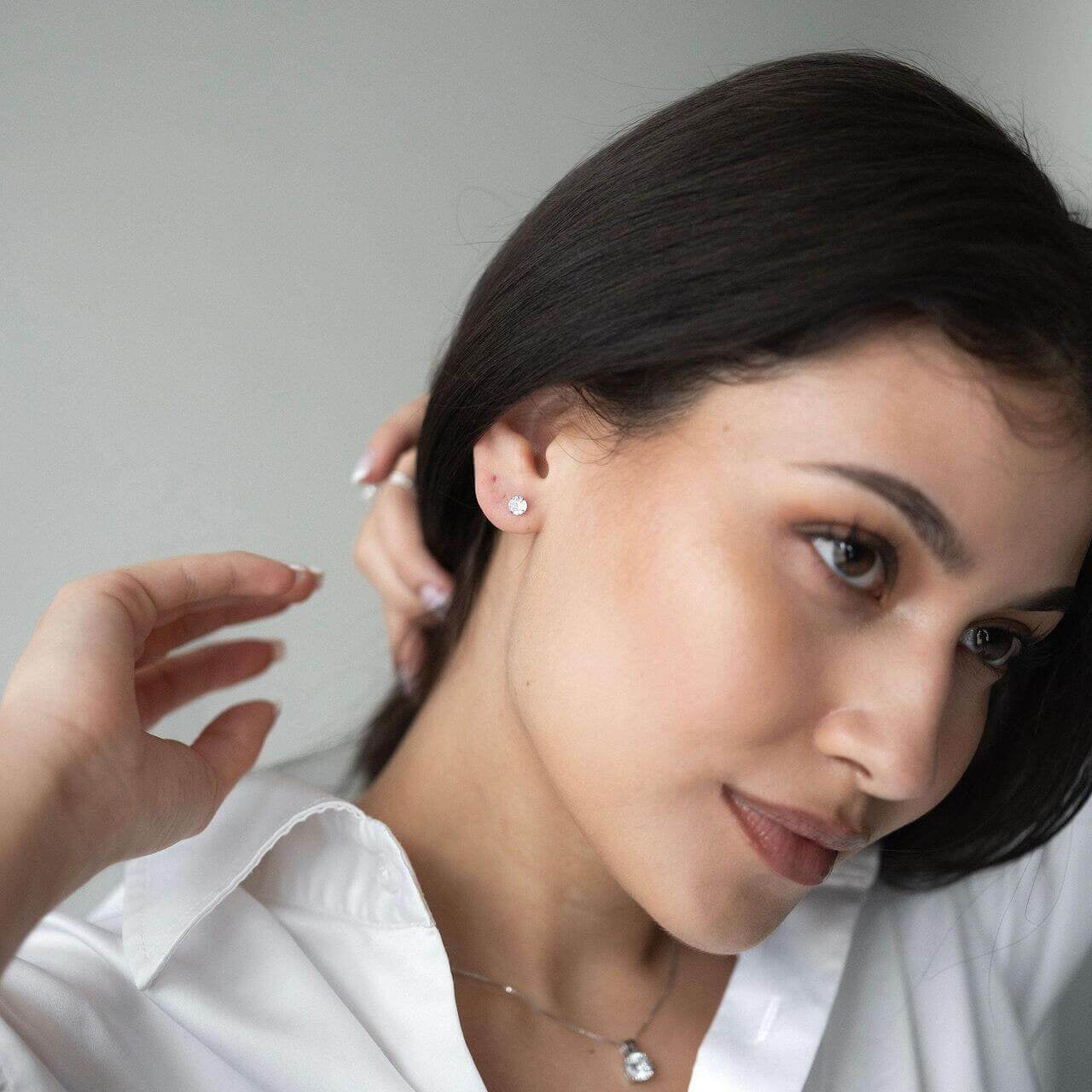 Млада жена с черна коса носи сребърни обеци Нежност S925, облечена с бяла риза.