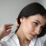 Млада жена с черна коса носи сребърни обеци Нежност S925, облечена с бяла риза.