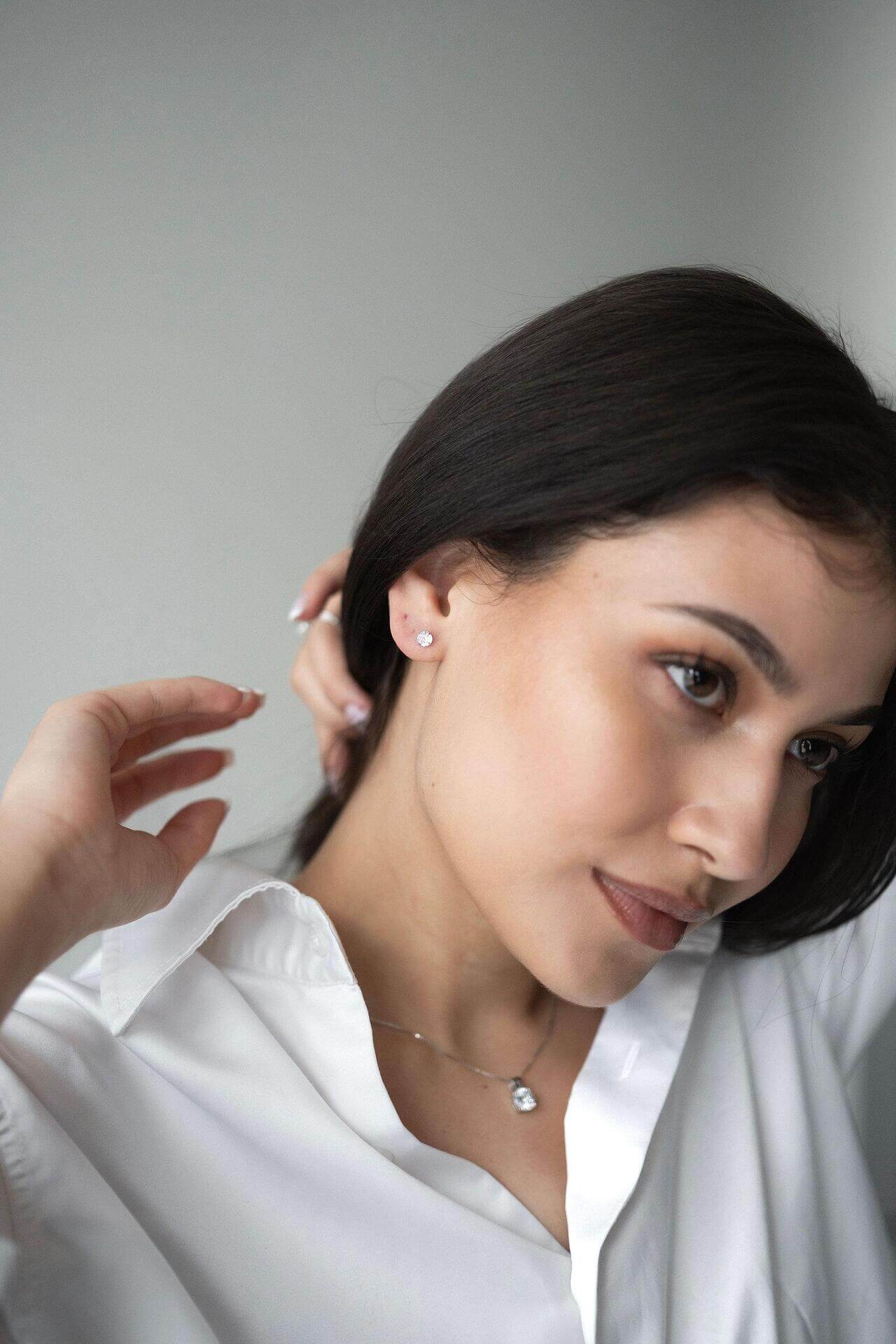 Млада жена с черна коса носи сребърни обеци Нежност S925, облечена с бяла риза.
