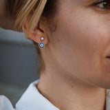 Сребърни обеци с окото на Хамса S925, носени от жена, излъчваща стил и символика.