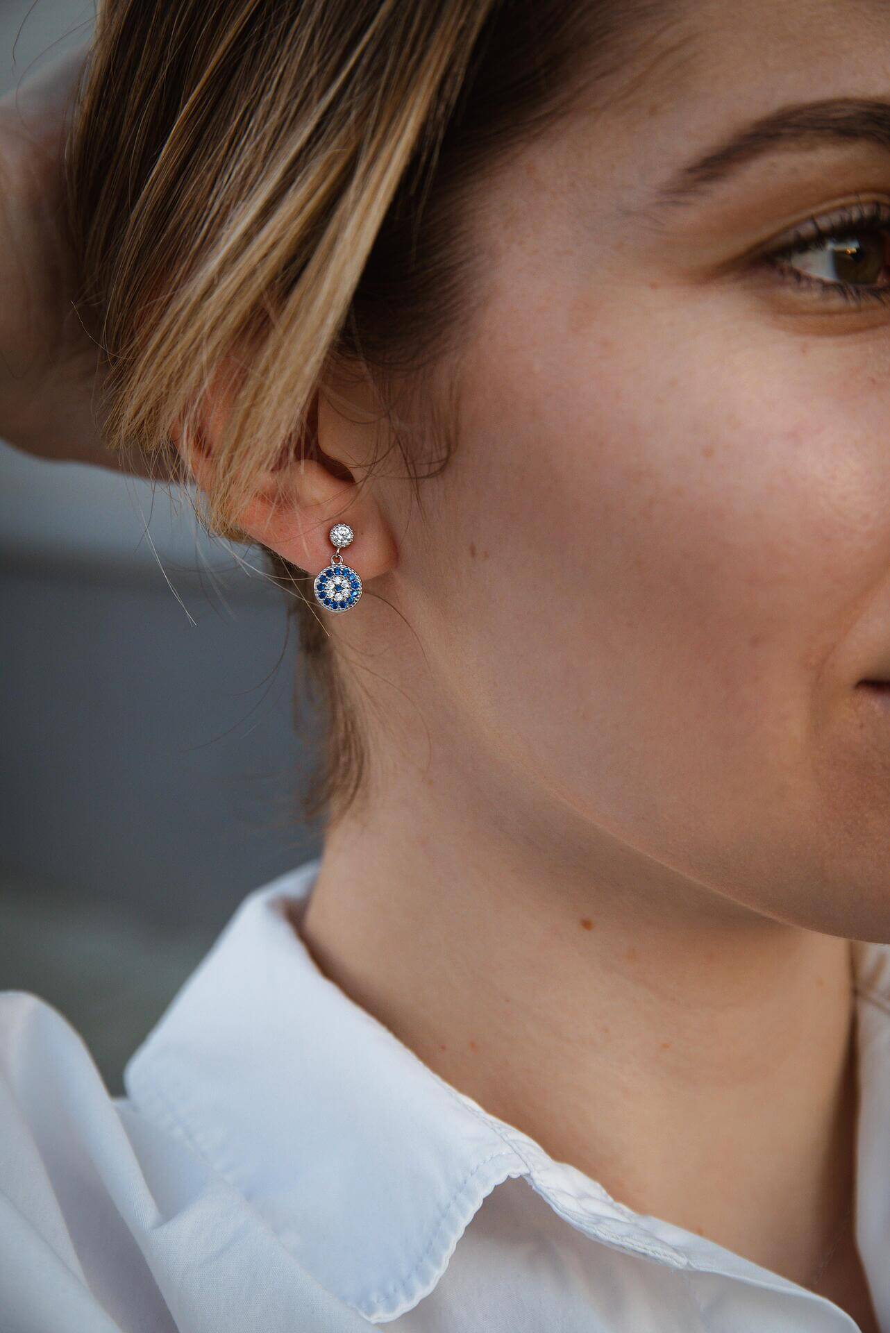 Сребърни обеци с окото на Хамса S925, носени от жена, излъчваща стил и символика.