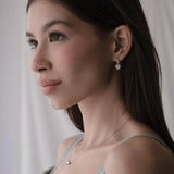 Дама с елегантни обеци във формата на сърце, с изразителен поглед и романтичен стил.