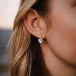 Елегантни сребърни обеци с форма на сърце, носени от жена с дълга коса на фон на залез.