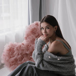 Млада жена сива блуза и дънки, усмихната на легло с розов сърцевиден възглавница.