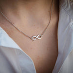 Сребърно елегантно колие безкрайност S925 на нежна дама, носеща бял риза, символизираща вечна любов.