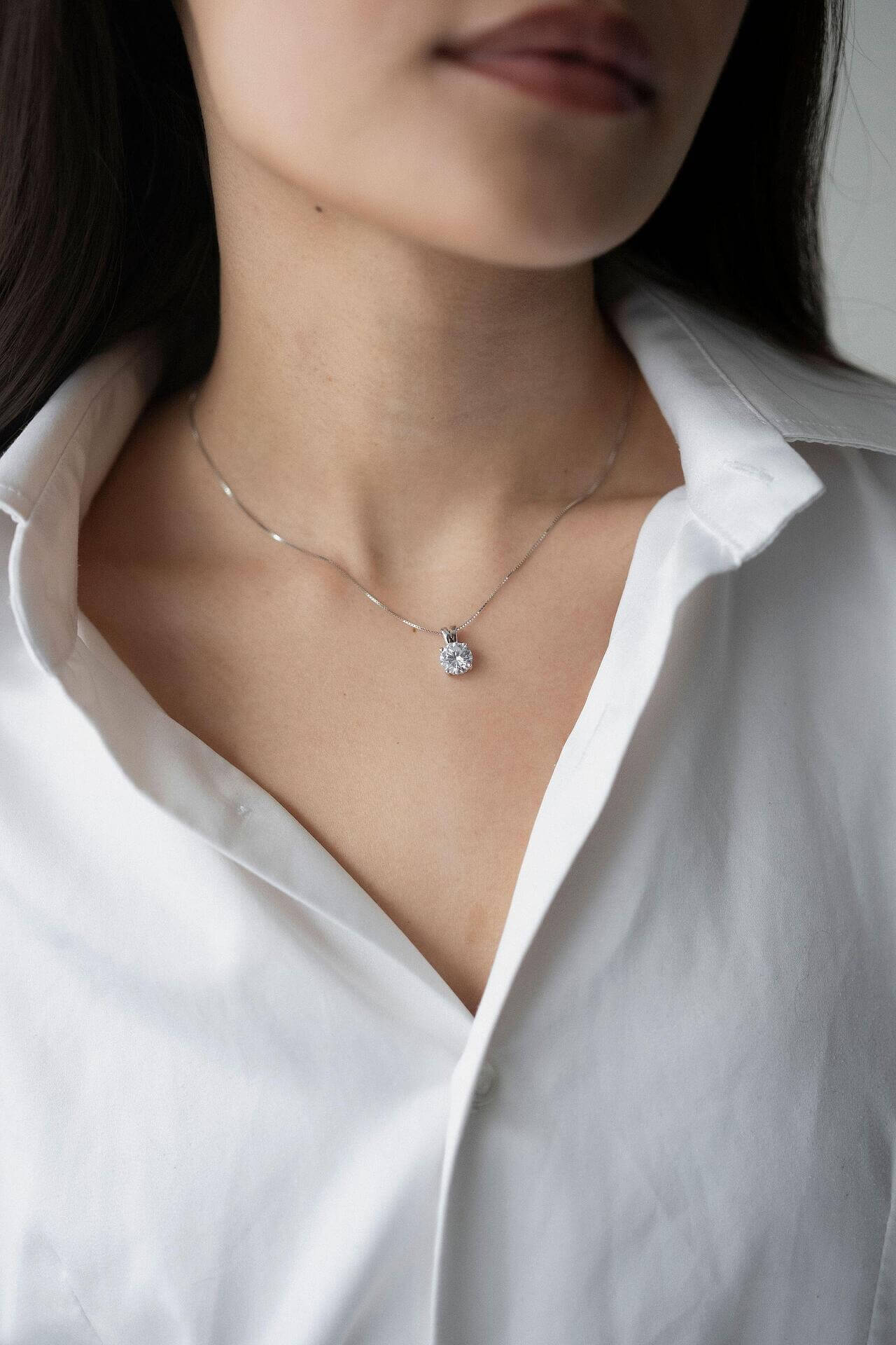 Сребърно колие S925 с цирконов камък, носено върху бяла риза, близък план на шията.