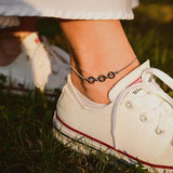 Модерна гривна за глезен от медицинска стомана с черни перли, носена с бели маратонки на зелена трева.