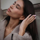 Модерна жена с дълга коса, носеща златисти обеци "Хибрид" с 18K златно покритие.