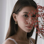 Жена с обеци сърце от 18K златно покритие, зад която се виждат червени цветя.