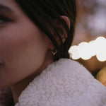 Златисти обеци с многонюансни кристали, носени от жена в уютно облекло, с ненатрапчив блясък.