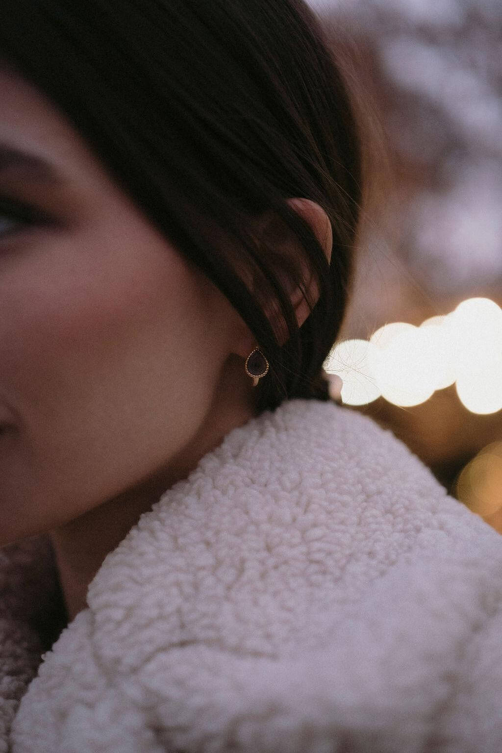 Златисти обеци с многонюансни кристали, носени от жена в уютно облекло, с ненатрапчив блясък.