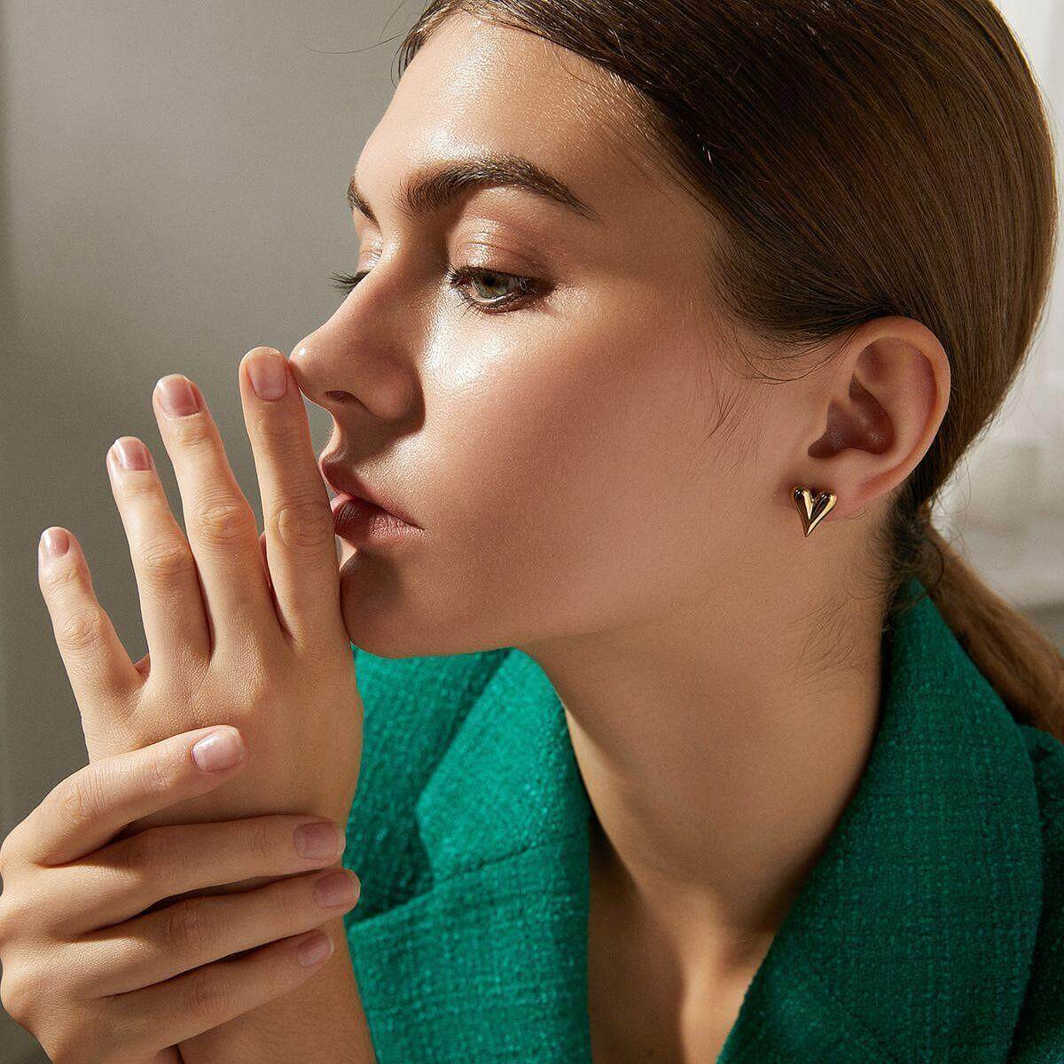 Златисти обеци модел Сърце, представени от жена с изтънчен стил и елегантен вид.