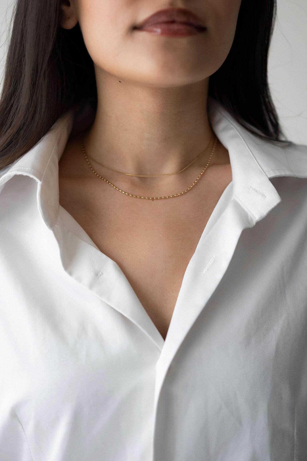 Златисто двойно колие Elara на нежна жена, облечена в бяла риза, изтъкваща елегантния дизайн.